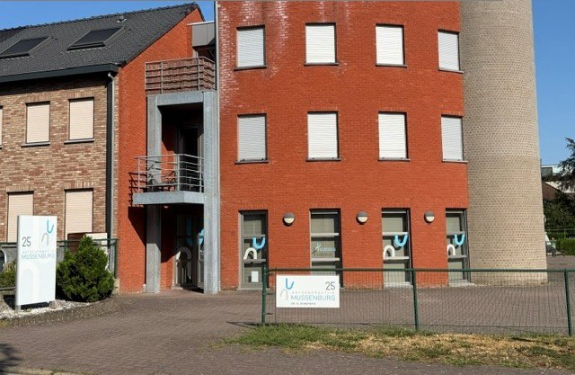 Het gebouw op Mussenburgstraat 25: een rood bakstenen pand van drie verdiepingen, met aan de straatkant twee witte borden met het logo van Artsenpraktijk Mussenburg en het huisnummer 25.
